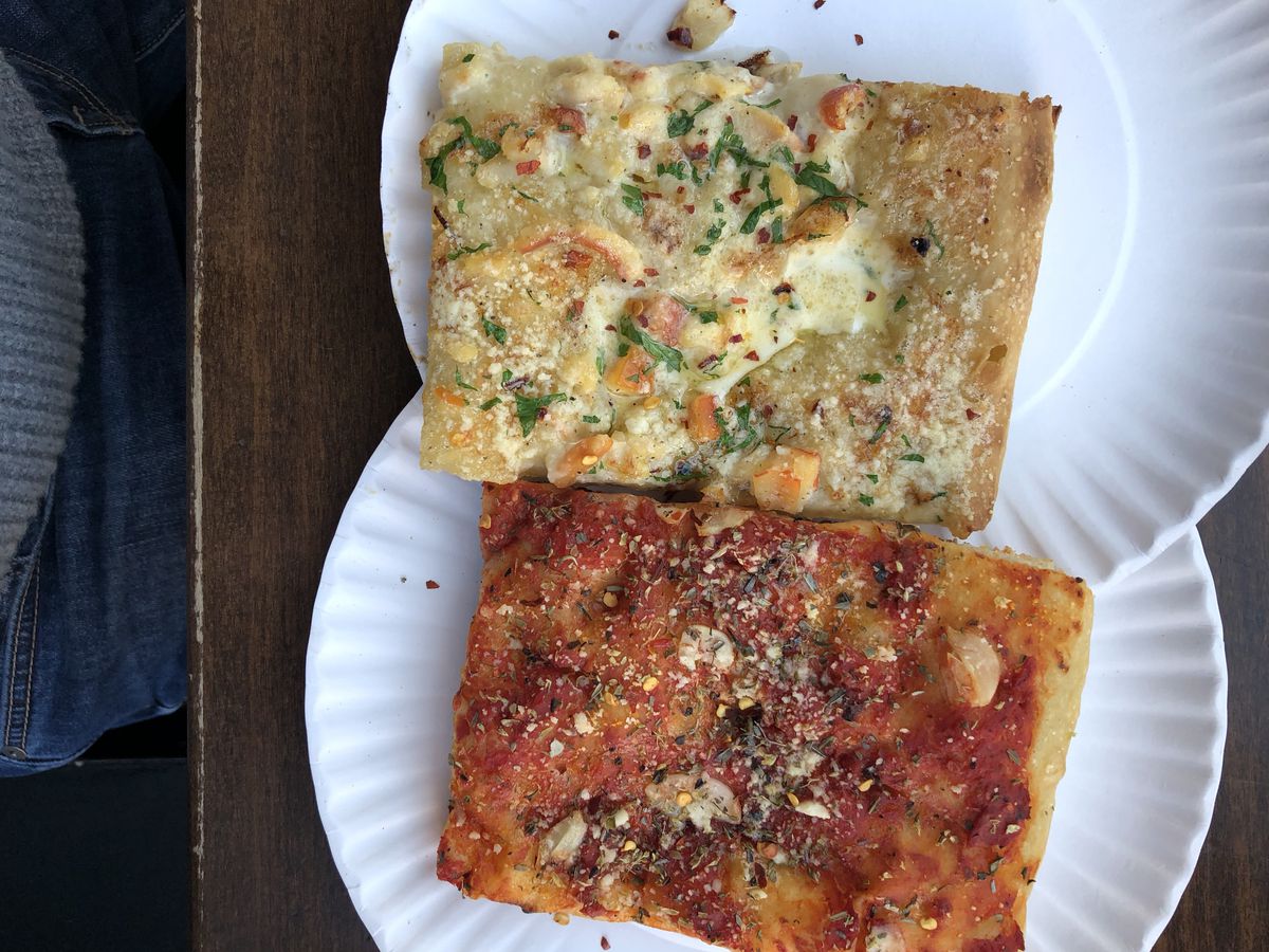 A white clam slice and a red tomato slice sit on paper plates at Gotham West Market