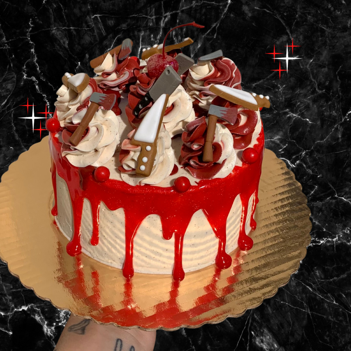 A white cake on a gold platter with red dripping icing topped with knife cookies and hatchet cookies.