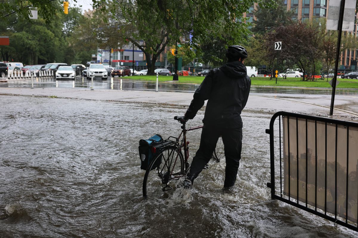 A person walks their bike through ankle-deep water along a flooded road near Prospect Park amid a coastal storm on September 29, 2023, in the Flatbush neighborhood of Brooklyn in New York City.
