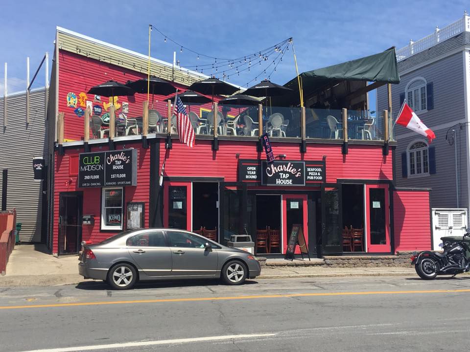 Red exterior of a one-story bar with umbrella-bedecked roofdeck, photographed during the day. Signage reads Charlie’s Tap House.