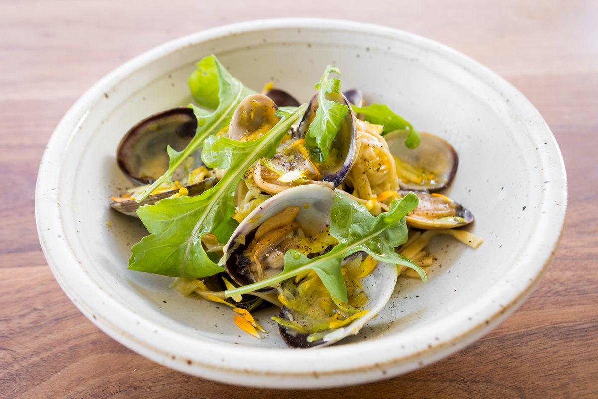 A shallow bowl filled with pasta, clams, and a few pieces of arugula.