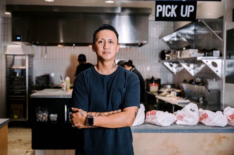 A chef stands with his arms folded in front of an open kitchen.