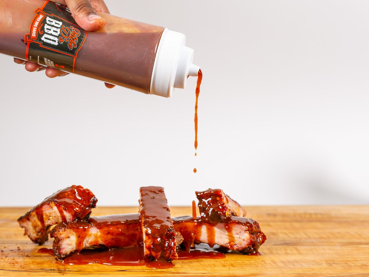 Barbecue sauce being squeezed onto a pile of ribs. 