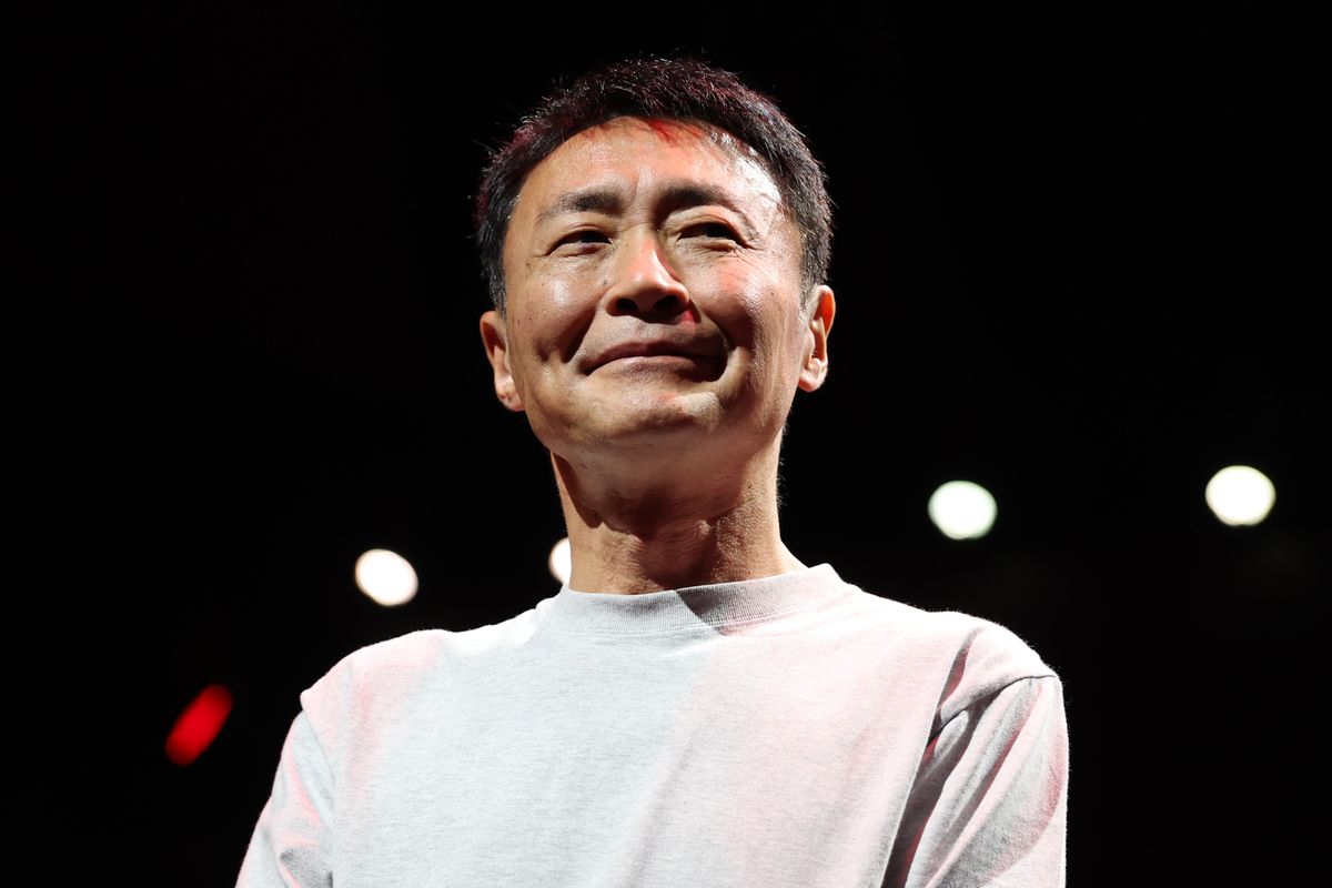 Gran Turismo creator Kazunori Yamauchi is pictured smiling in a white sweater against a dark background