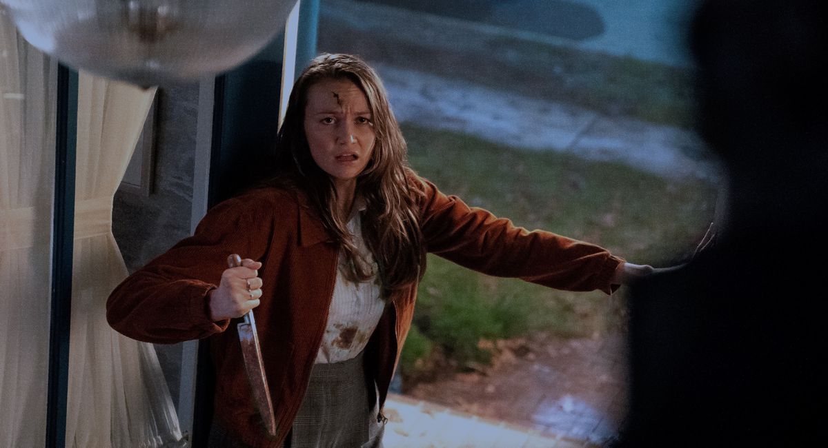 A bloodied woman wielding a knife faces a looming Shape in Halloween Kills