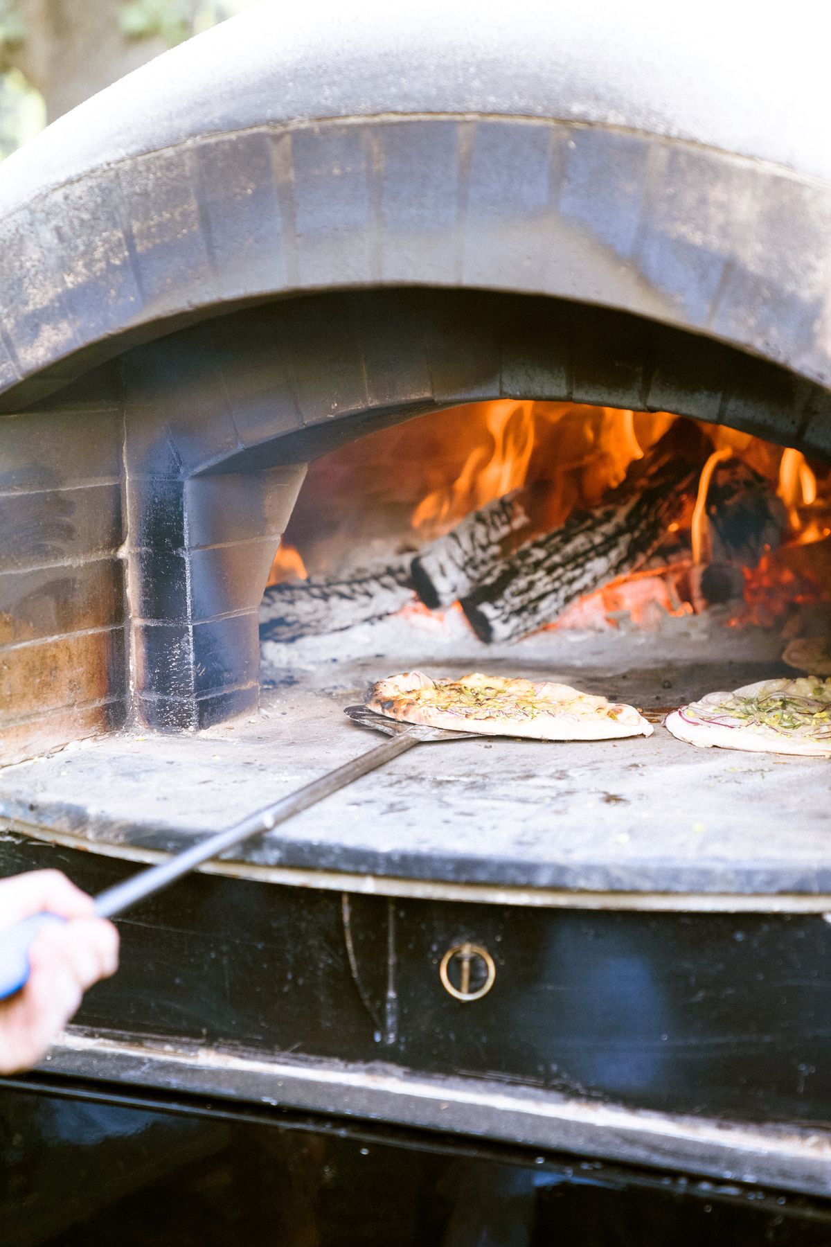 A pizza being put into an outdoor oven.
