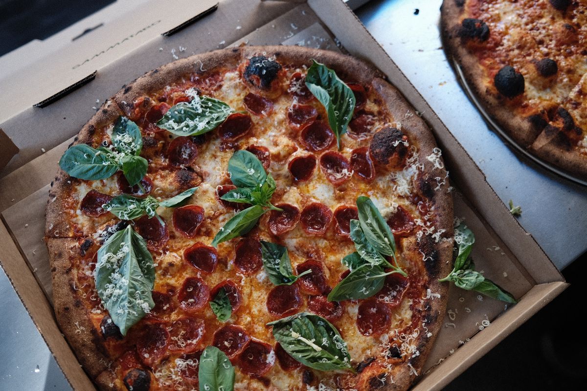 Pepperoni pizza with lots of basil in a cardboard pizza box