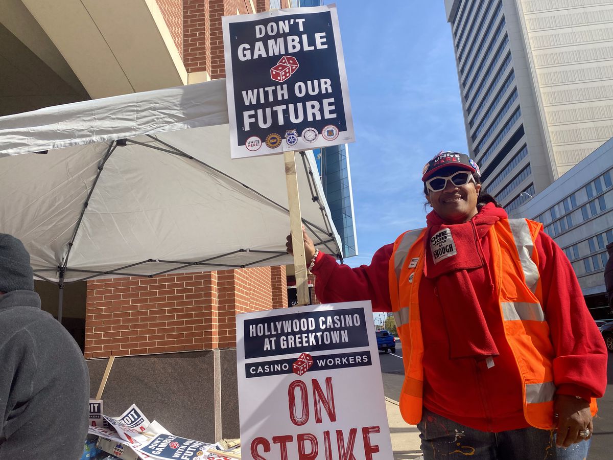 Alicia Weaver, a guest room attendant at MGM Grand Casino in Detroit, is picketing outside of Hollywood Casino at Greektown on October 18, 2023, day 2 of the casino workers strike, carryign a sign, wearing sunglasses, and an orange vest.