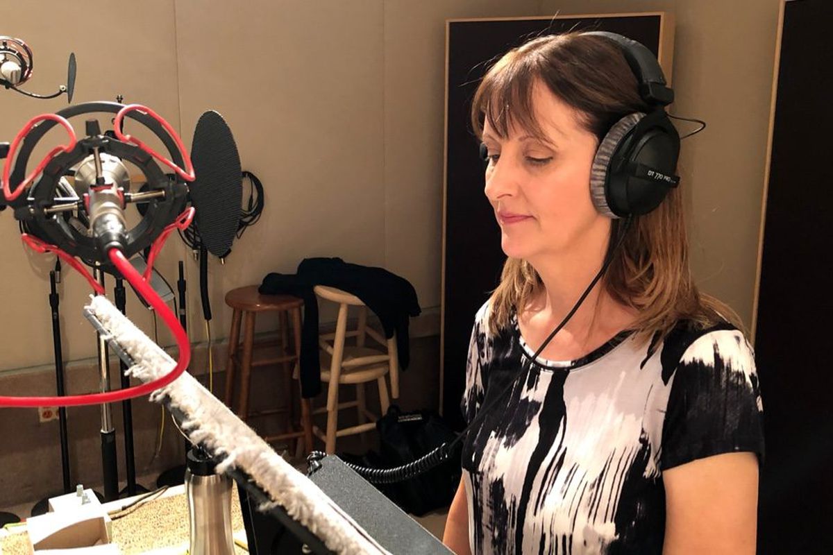Voice actor Kia Huntzinger looks at her script as she reads lines into a studio microphone