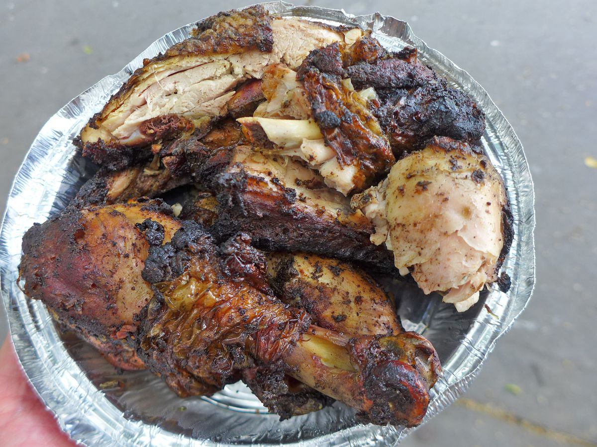 A round foil container of chicken blackened and chopped up into irregular pieces.