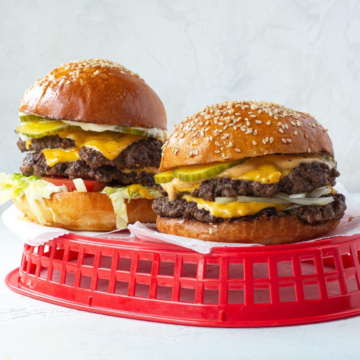 Two double cheeseburgers with pickles, onions, lettuce, and tomato atop an upside down red basket