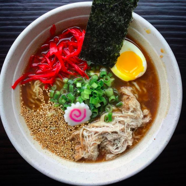 overhead view of ramen with green onions, red pickled ginger, half a hard-boiled eggs and a slice of a pink and white swirled fish cake