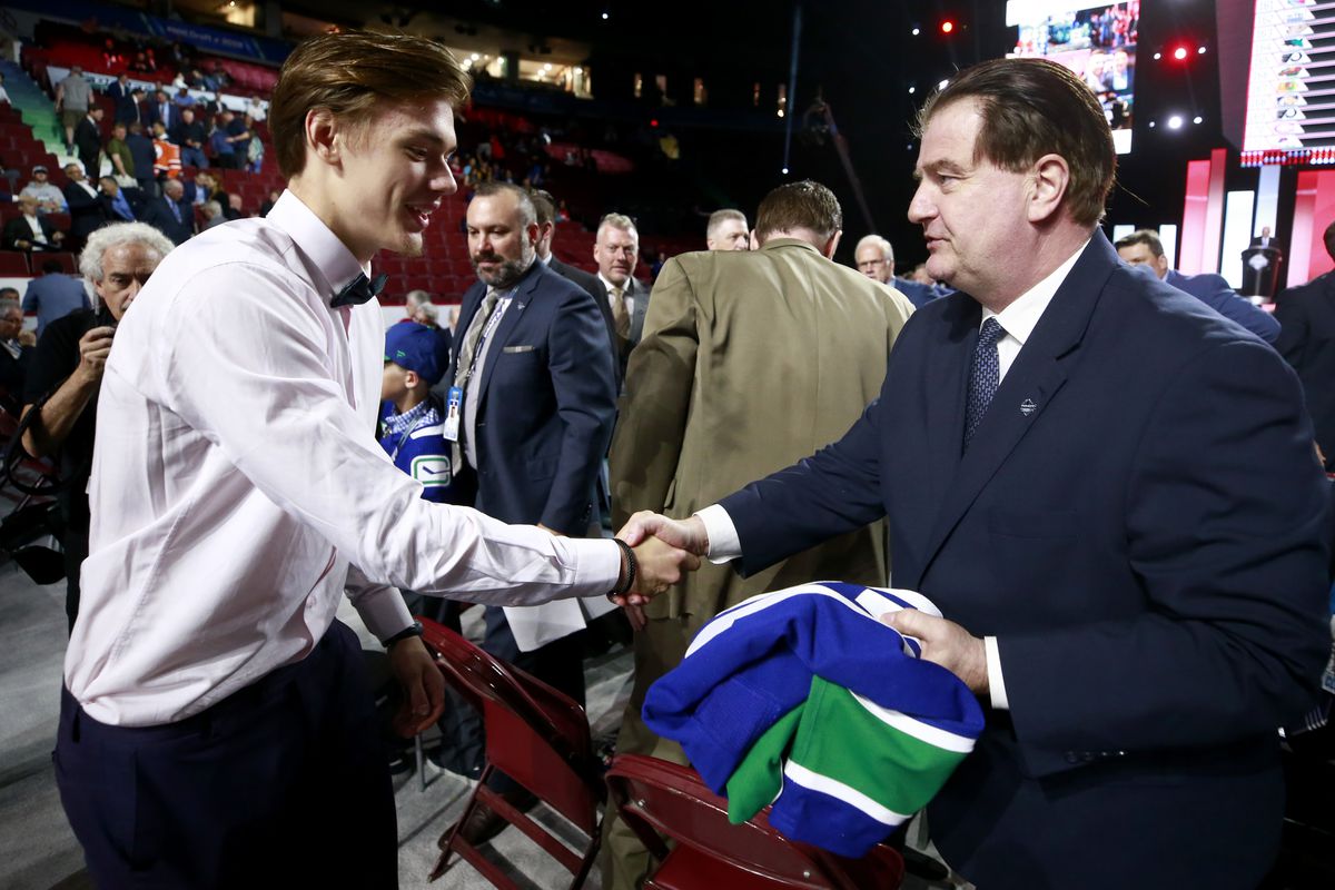 Arturs Silovs, 156 pick overall of the Vancouver Canucks, is greeted by general manager Jim Benning of the Vancouver Canucks on the draft floor during Rounds 2-7 of the 2019 NHL Draft at Rogers Arena on June 22, 2019 in Vancouver, Canada