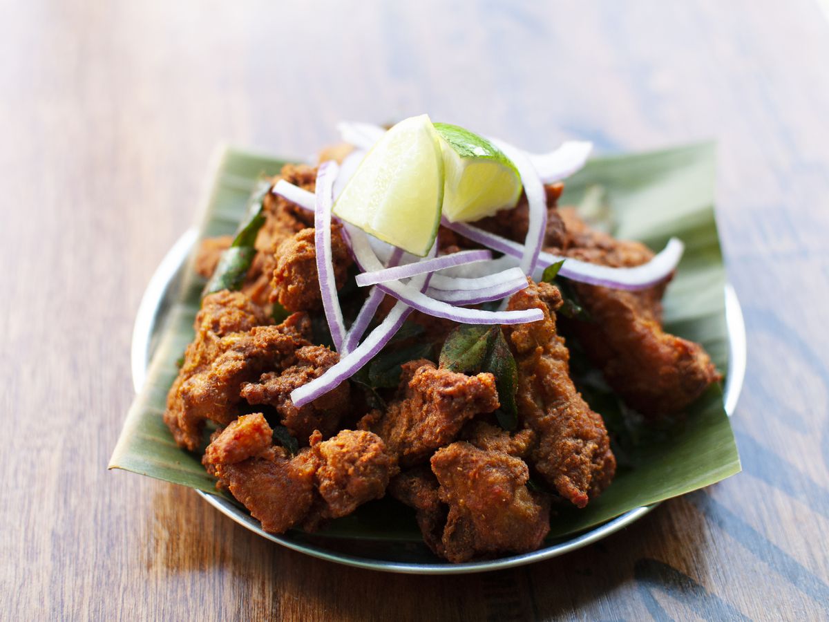 A pile of fried chicken pieces served on a leaf and topped with sliced red onion and lime wedges.