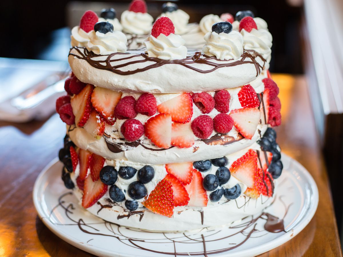 A tall meringue cake is layered with berries, whipped cream, and chocolate drizzle at Papa Haydn.