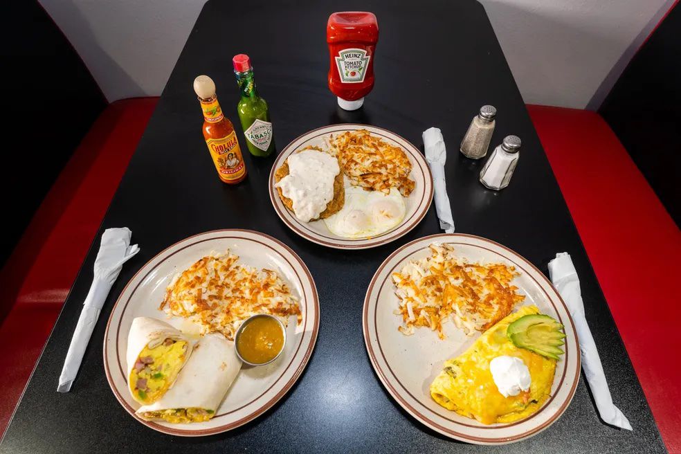 Three white plates withe a breakfast burrito, omelet, and chicken fried steak on a black table. 
