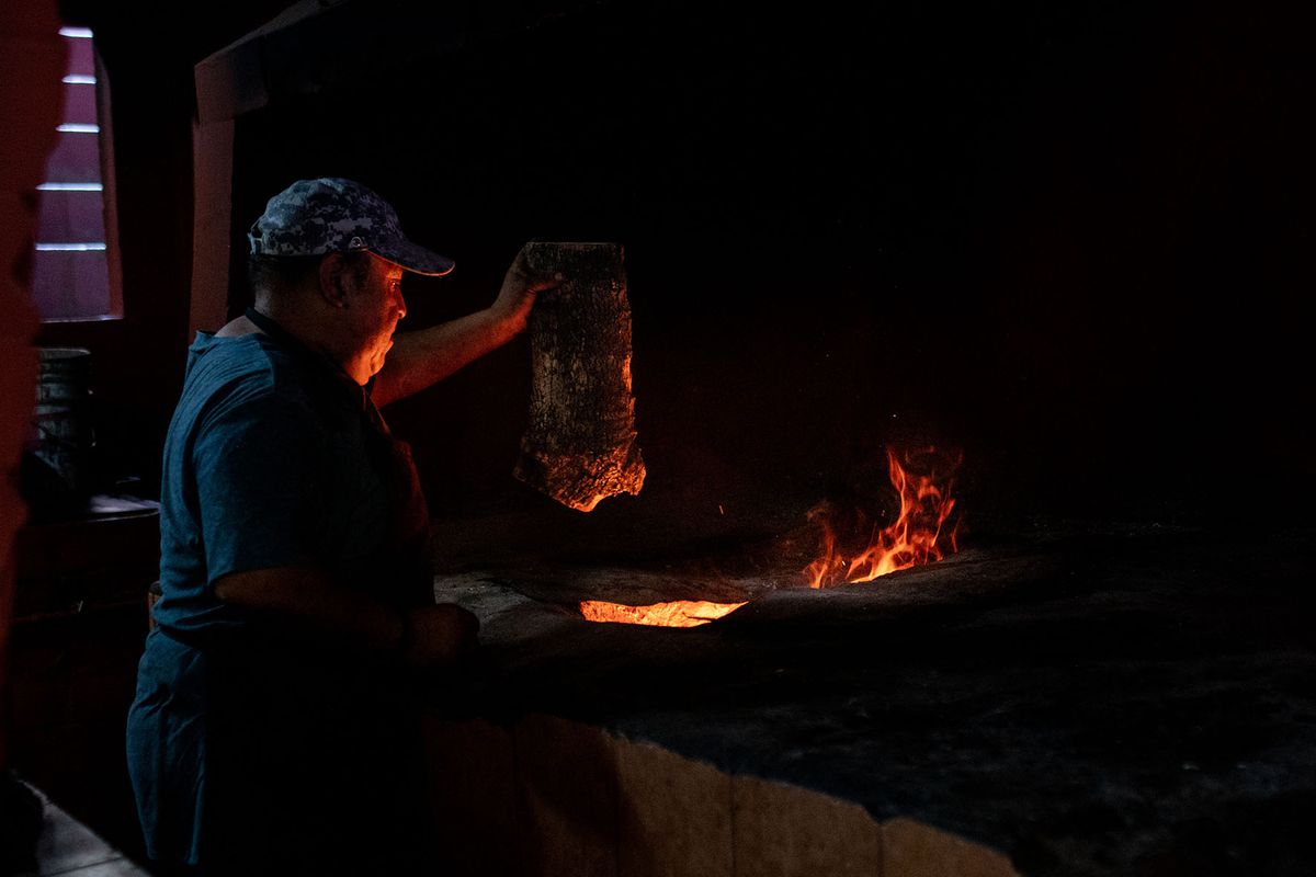 A cook holds a large chunk of meat, ready to drop it into a fiery pit.