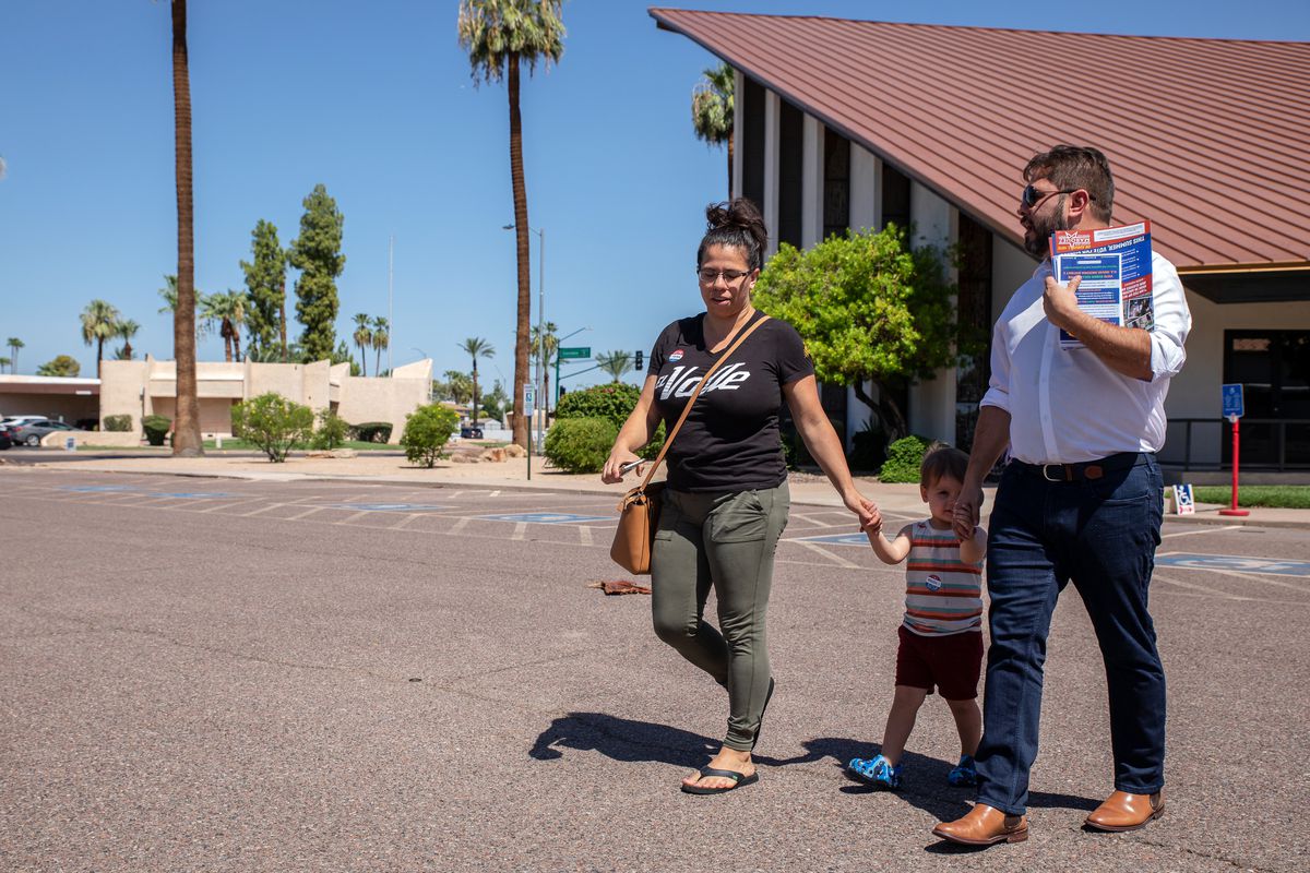 Gallego and a woman walk hand in hand with a child between them across a parking lot.