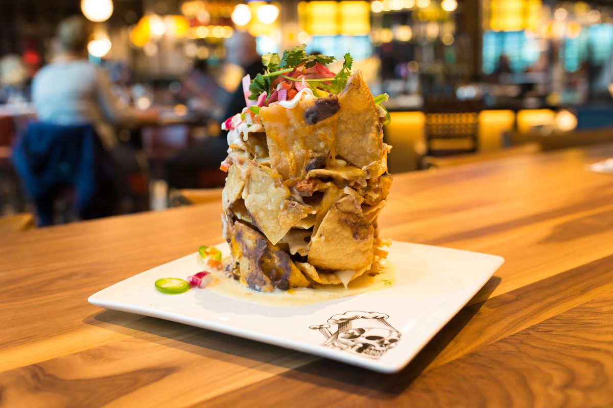 A pile of “trash can nachos” on a white plate on a wooden table in a restaurant
