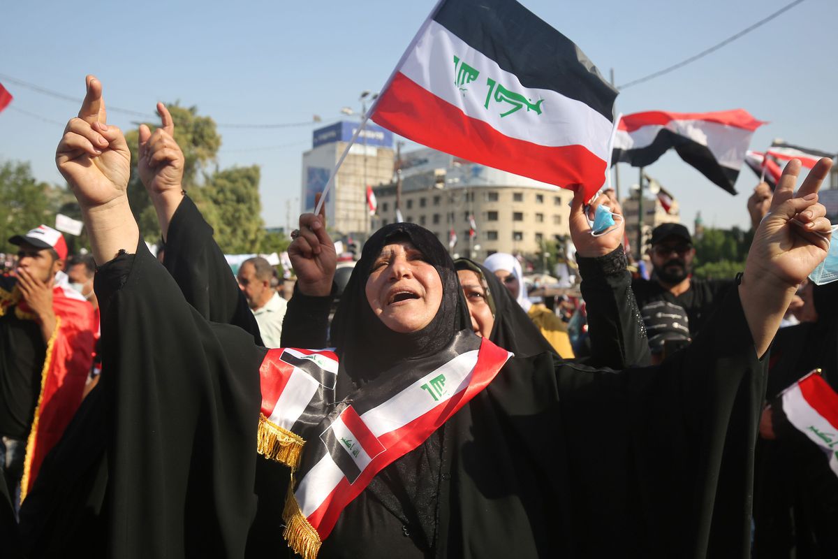An Iraqi protester in a burqa raises their arms while others wave flags in Baghdad’s Tahrir Square.