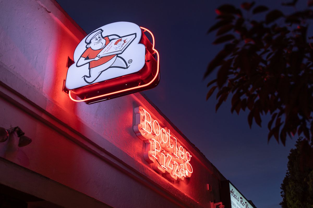 A neon sign, lit at night, for a new pizza restaurant, with the logo of a man holding a box.