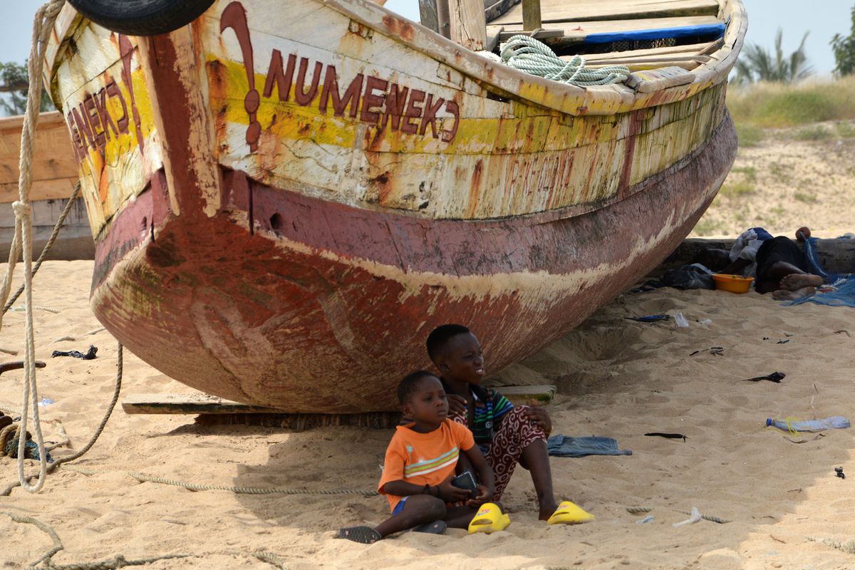 Two little boys watch attentively as dozens of men pull one of the giant fishing canoes on shore in the Lake Volta Region of Ghana. 