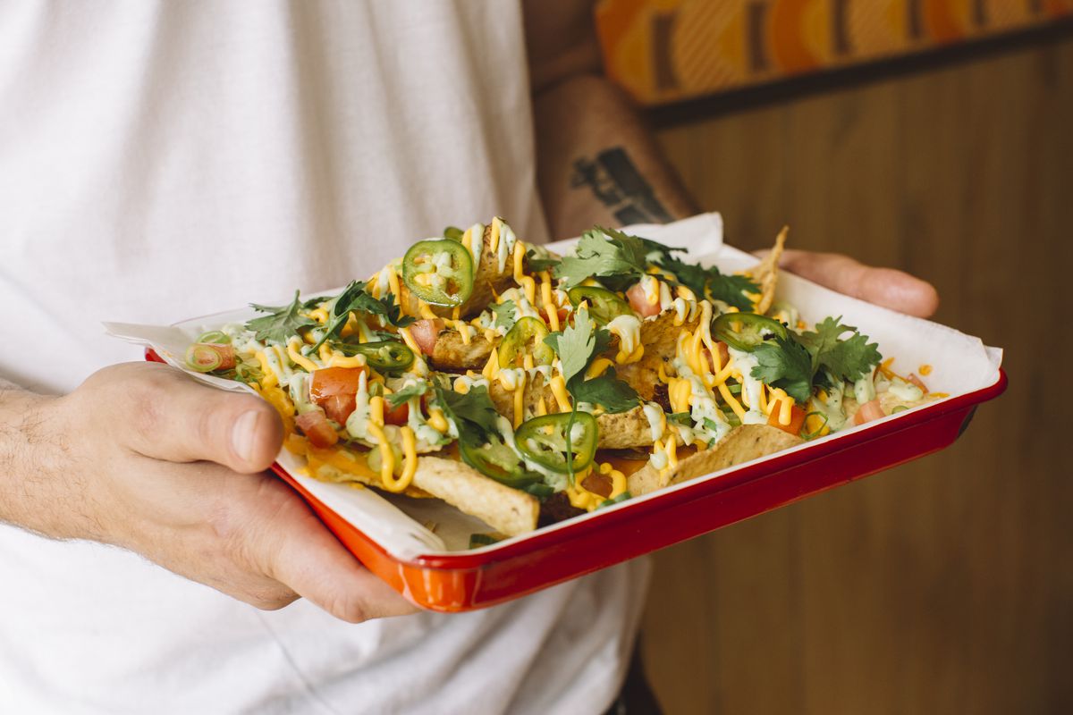 A man holds a red tray filled with nachos