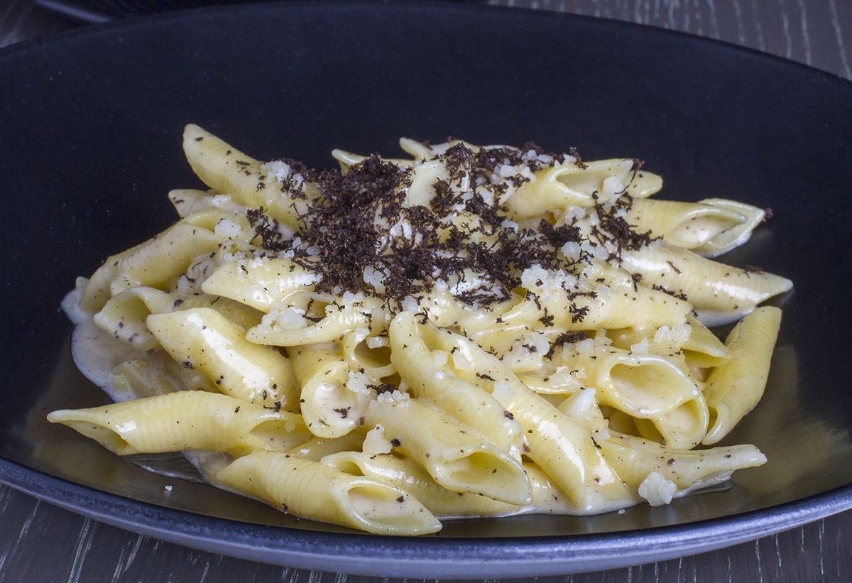 A plate of garganelli pasta covered in butter sauce and truffle shavings.