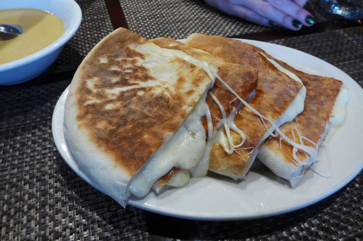 A cheese filled flat bread cut in quarters and stacked on the place, oozing cheese.