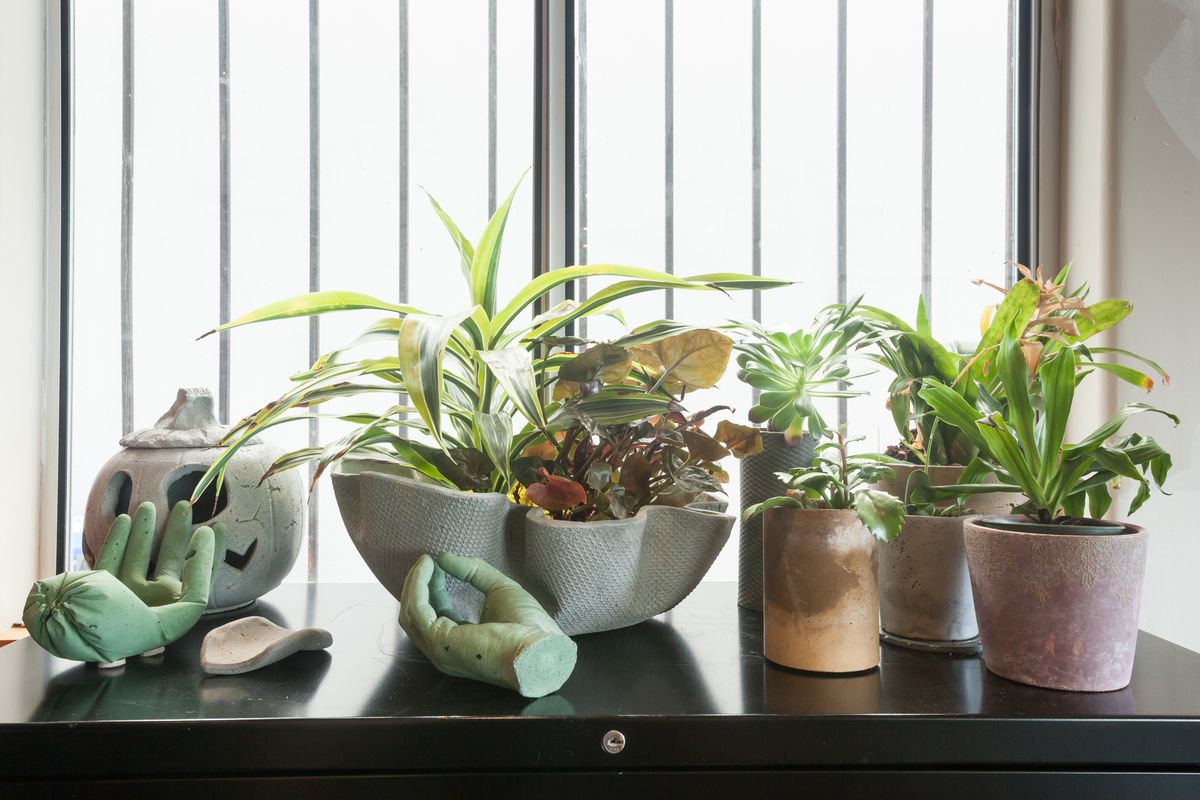 Several small objects, mostly planters, made out of concrete sit on a table in front of a window.