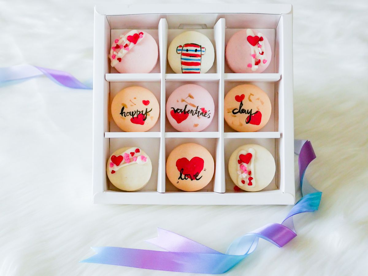 A segmented box of Valentine’s Day themed macarons in white, red, and pink, with illustrated hearts and a toy monkey