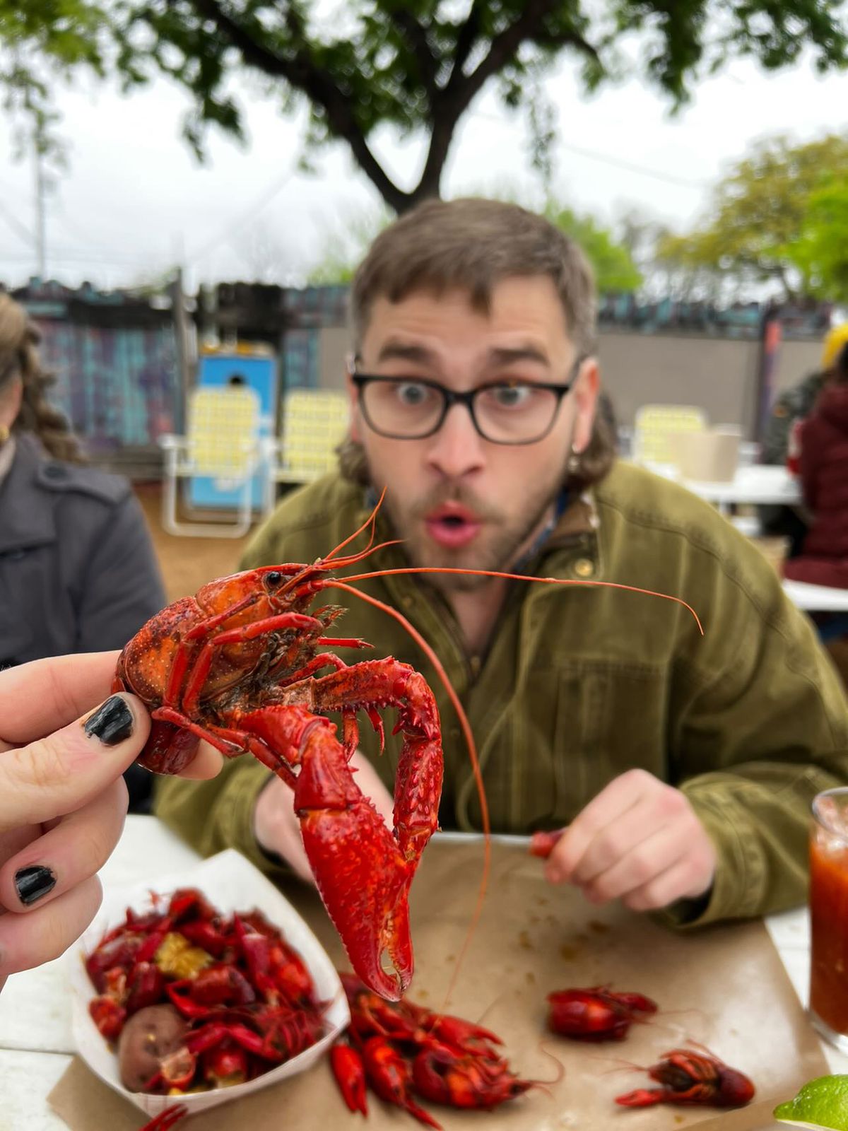 A person holding up a crawfish in front of another person.