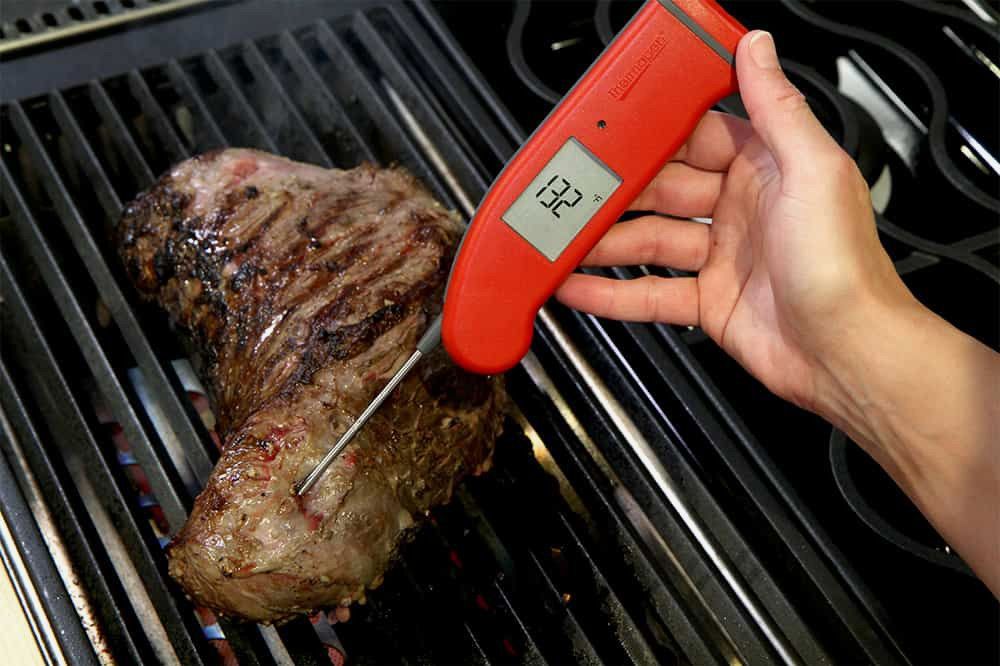 Person using a thermapen to check the temperature of a steak on a grill