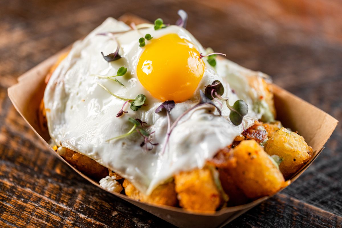 A paper basket holds tater tots covered with a sunny side up egg and salsa.