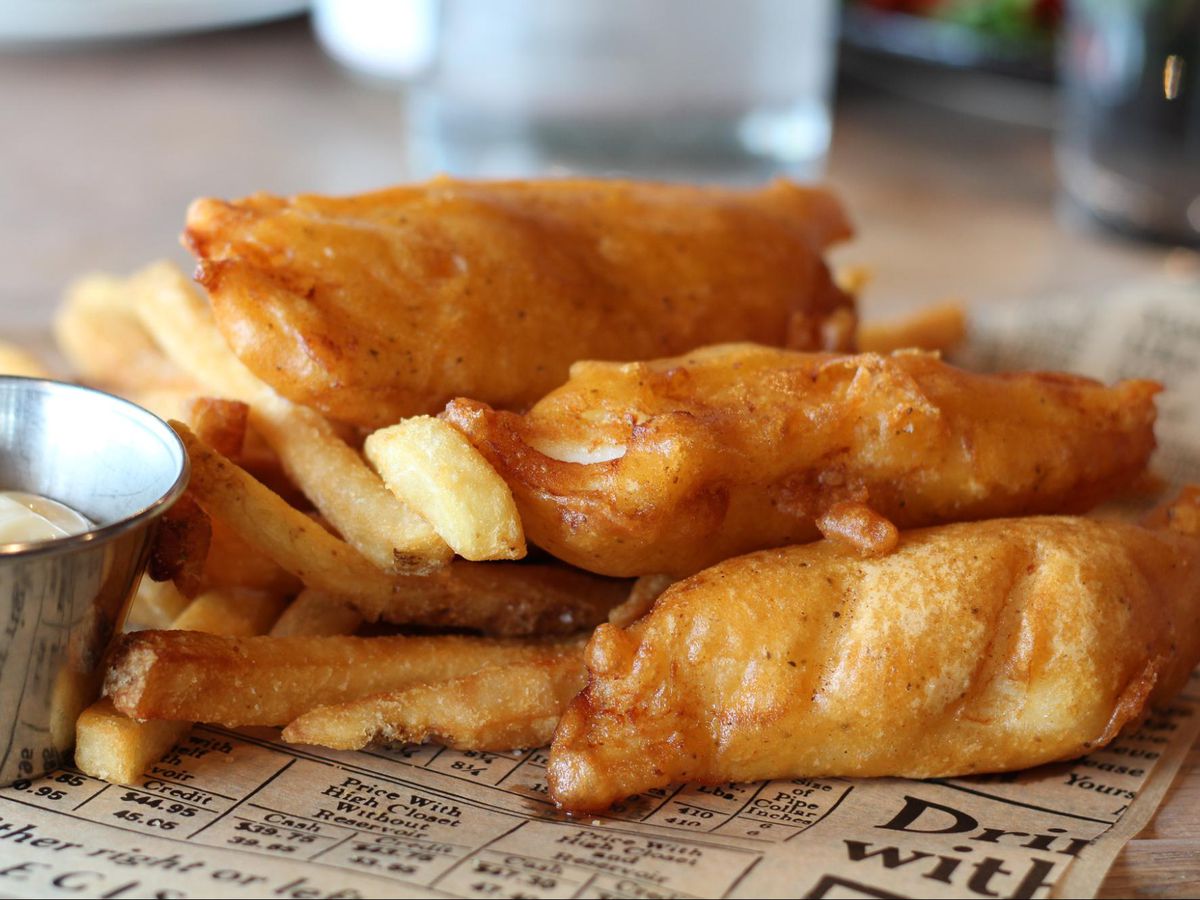 Three pieces of beer-battered fish and fries laid out on a newspaper.