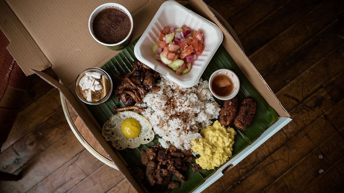 A top-down view of garlic fried rice, a sunny side up fried egg, mushrooms, vegetables, and a silken sweet desert, all in a large cardboard box.