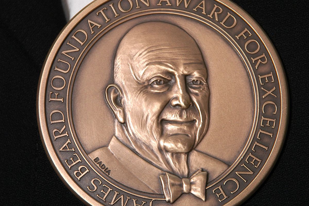 The James Beard award medal, cast in bronze, with the likeness of James Beard surrounded with the words “James Beard Foundation Award for Excellence” against a black background. 