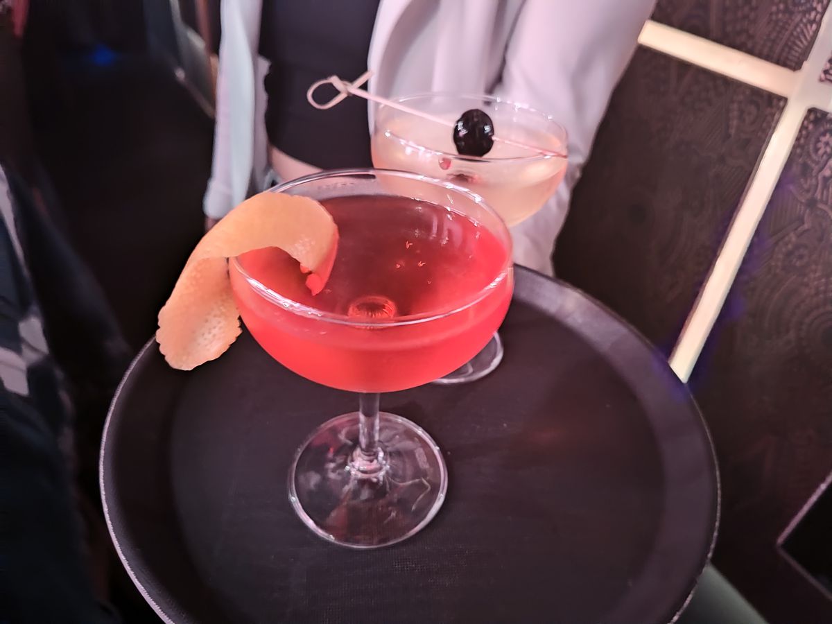 A server holding a black tray with two decorated cocktails. 