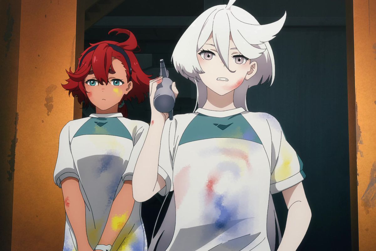 Suletta Mercury nervously stands behind Miorine, who’s holding an airbrush. Both are wearing matching paint-stained t-shirts in a scene from Mobile Suit Gundam: The Witch from Mercury.