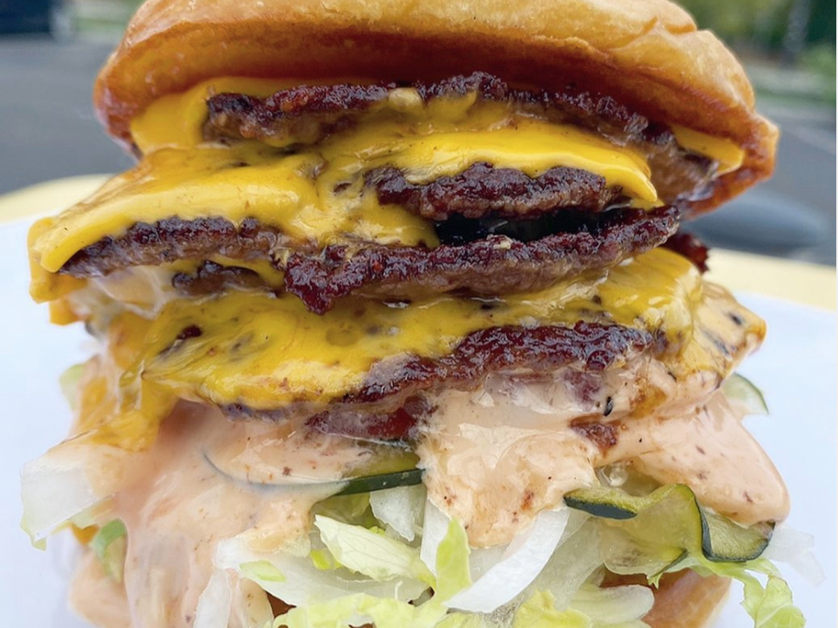 Four cheese-covered beef patties sit nestled on a bed of lettuce, pickles, and special sauce between two golden, toasted, buns.