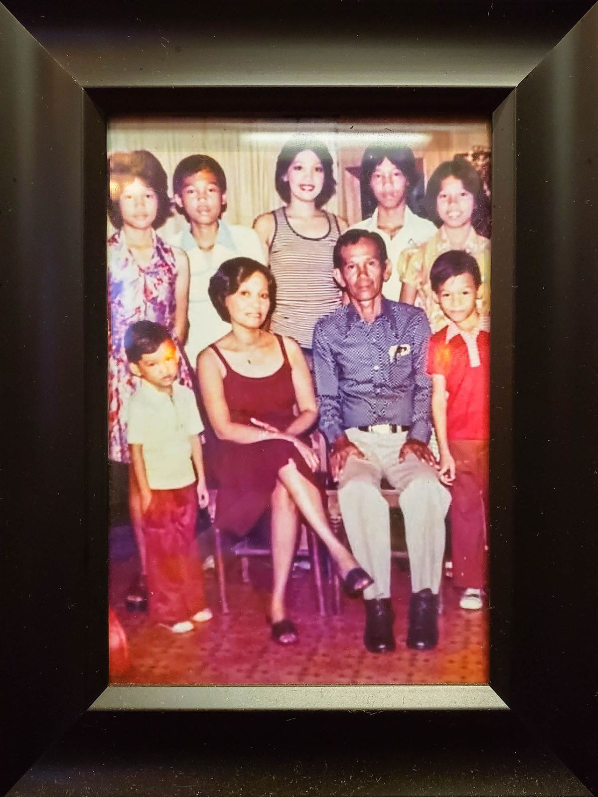 A thick black frame around an old photo of a Filipino family.