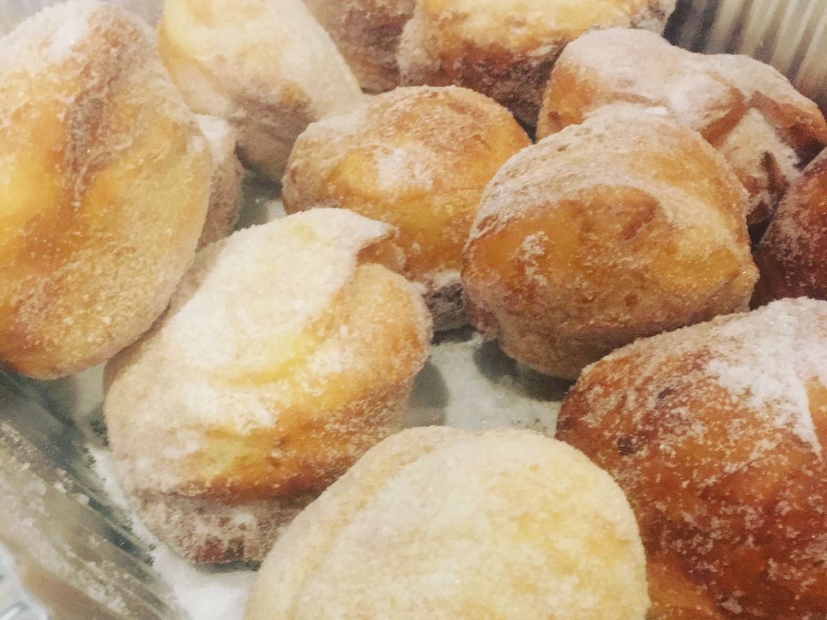 A bunch of sugar dusted paczki in a metal pan.