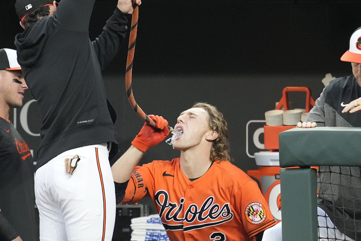 Orioles player Gunnar Henderson, in the team’s orange uniform top, drinks water from an orange and black hose to celebrate a home run.