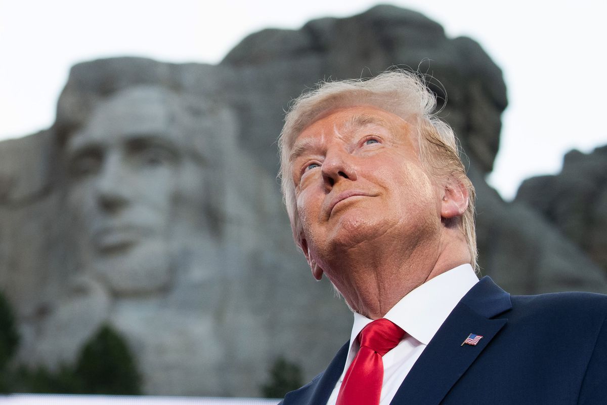 President Trump stands, smiling, with Mount Rushmore behind him.