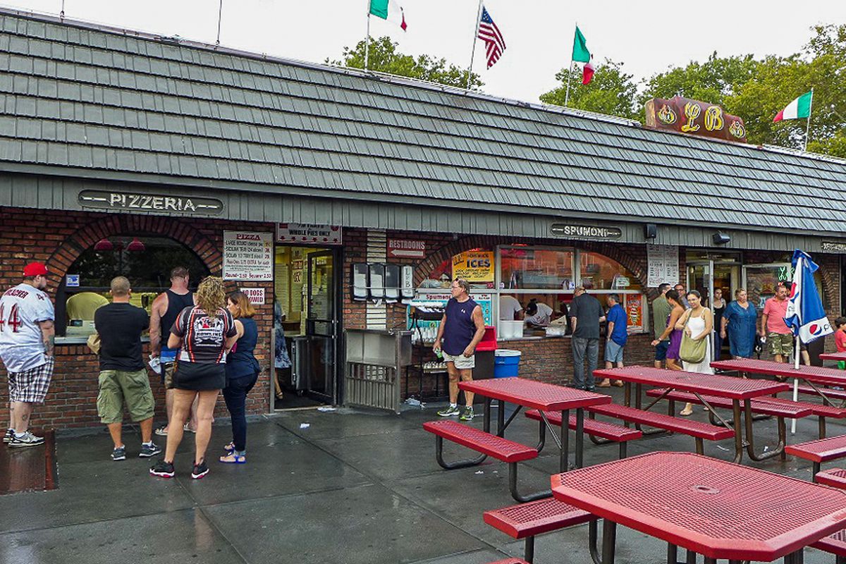L &amp; B Spumoni Gardens’s outdoor area has people lined up at a counter, with red tables.