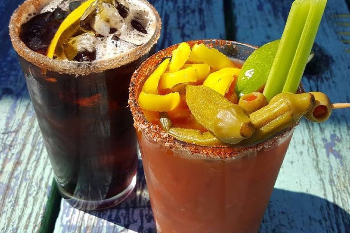 A dark brown beverage and red bloody mary topped with okra