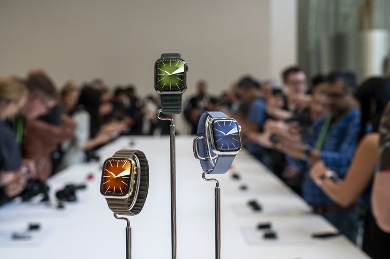 Three Apple Watches sit on pedestals in front of a crowd of people.
