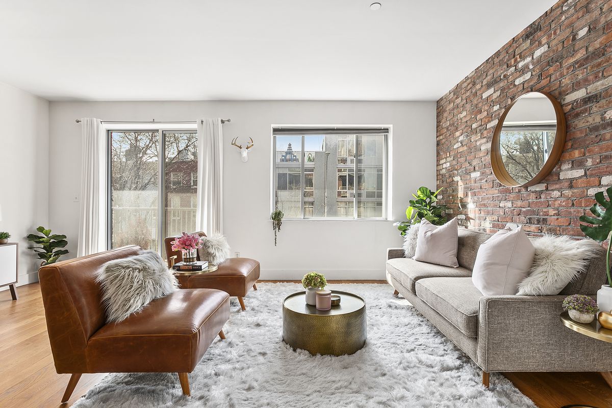 The living room has one exposed brick wall, one large window, and a sliding glass door that lets out onto a west-facing patio.
