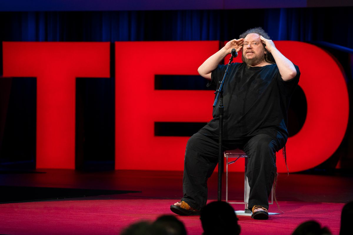 VR pioneer Jaron Lanier sits on the TED conference stage in front of the letters T, E D