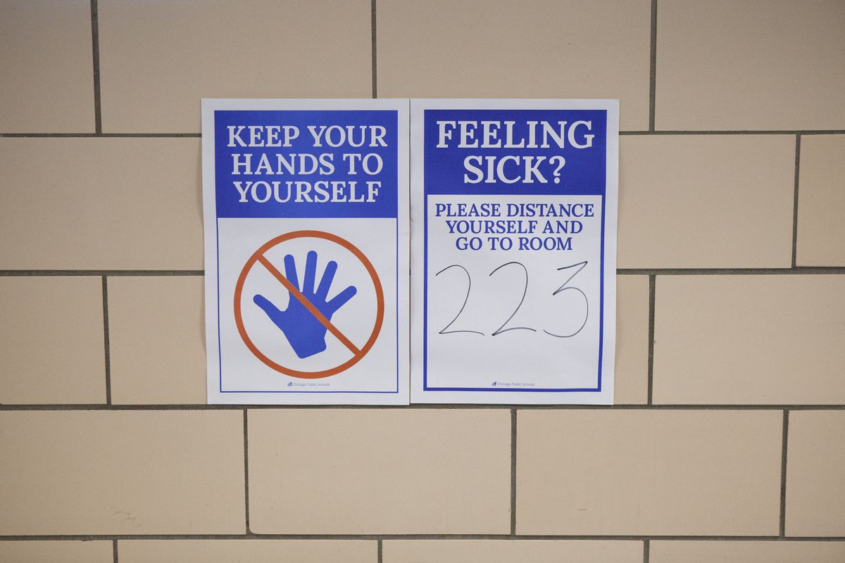 Posters in school hallway reminding students to keep their hands to themselves and stay distant if feeling sick.